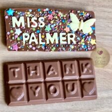A milk chocolate bar, topped with solid white chocolate butterflies and colourful sugar sprinkles. Teachers name is in white chocolate letters and the back of the bar says 'thank You'