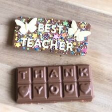 Best teacher milk chocolate bar, topped with solid white chocolate butterflies and sprinkles. The back of the bar says 'Thank You'