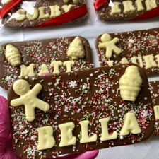 A milk chocolate bar topped with recipients name, festive chocolate shapes and sprinkles.