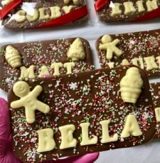 A milk chocolate bar topped with recipients name, festive chocolate shapes and sprinkles.